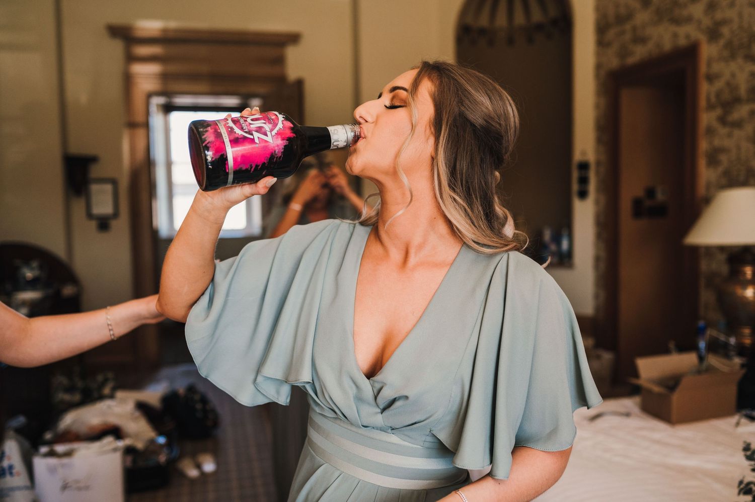 Someone in a light blue dress drinks from a can while getting ready in an elegant room.