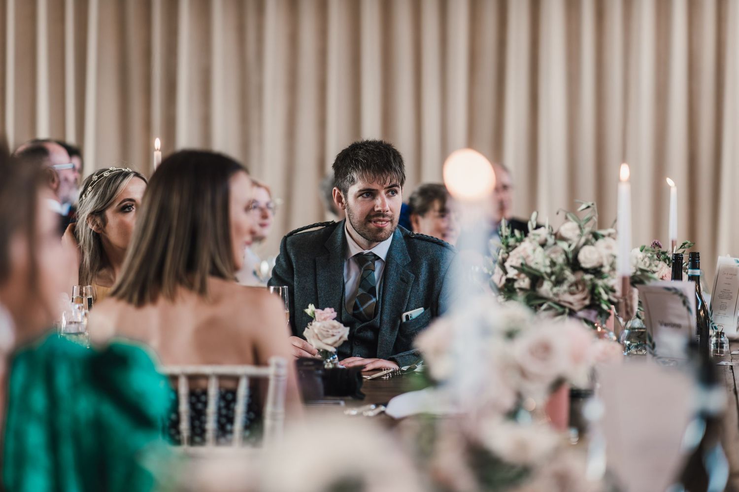 Wedding reception dinner scene with guests seated at decorated tables with floral centerpieces.