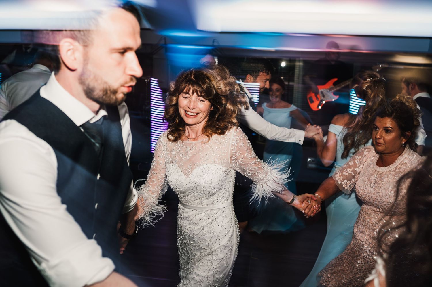 Wedding party dancing and holding hands during reception celebration.