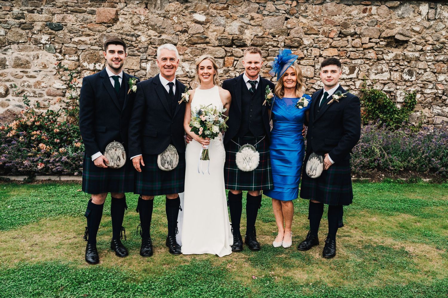 Wedding party in traditional Scottish kilts pose for formal group photo.