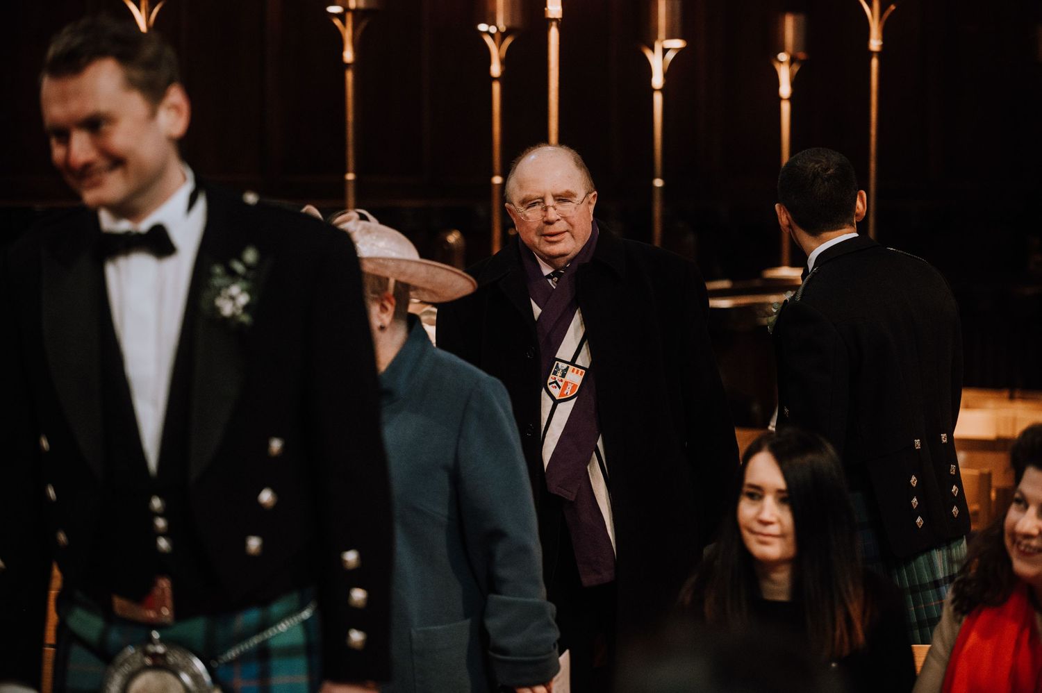 Candlelit church ceremony with traditional Scottish attire and formal wear.