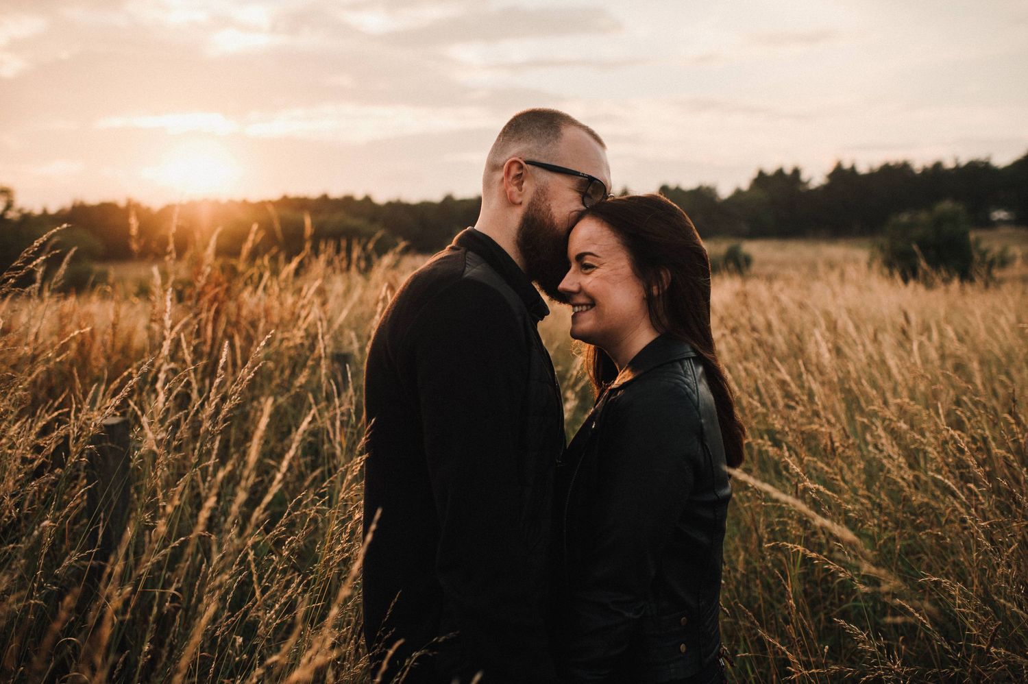 An intimate moment between a couple standing in tall grass during golden hour sunset.
