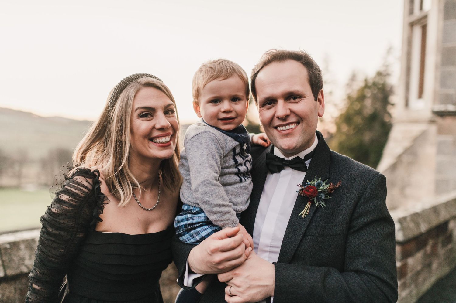 A joyful outdoor portrait at a formal event against a stone building backdrop.