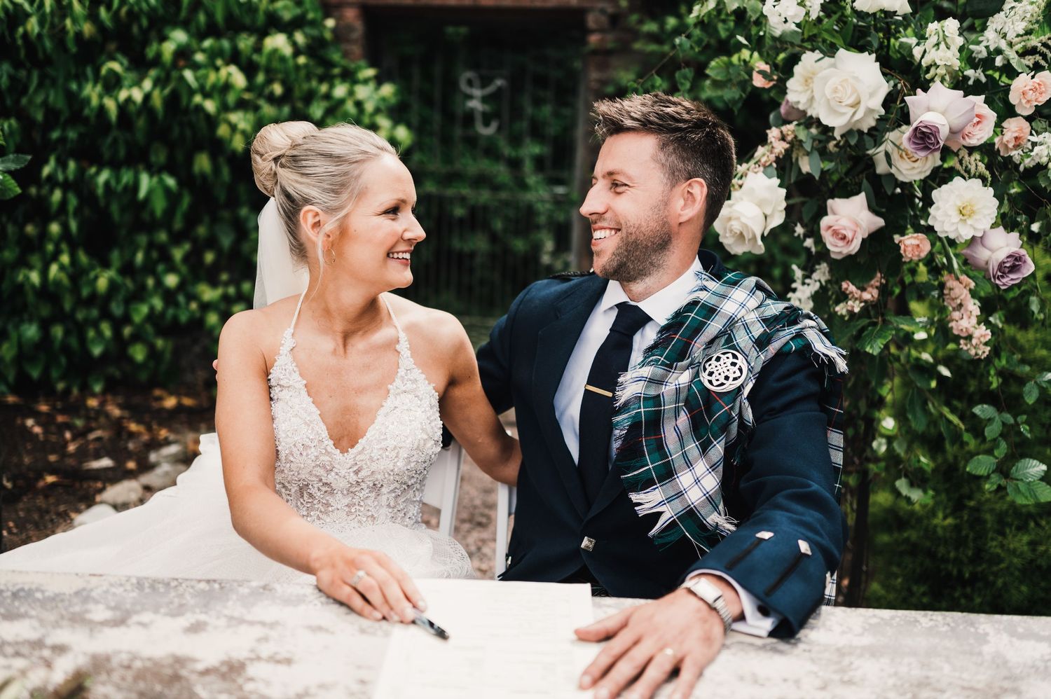 Candid moment between newlyweds at stone table during garden wedding reception.