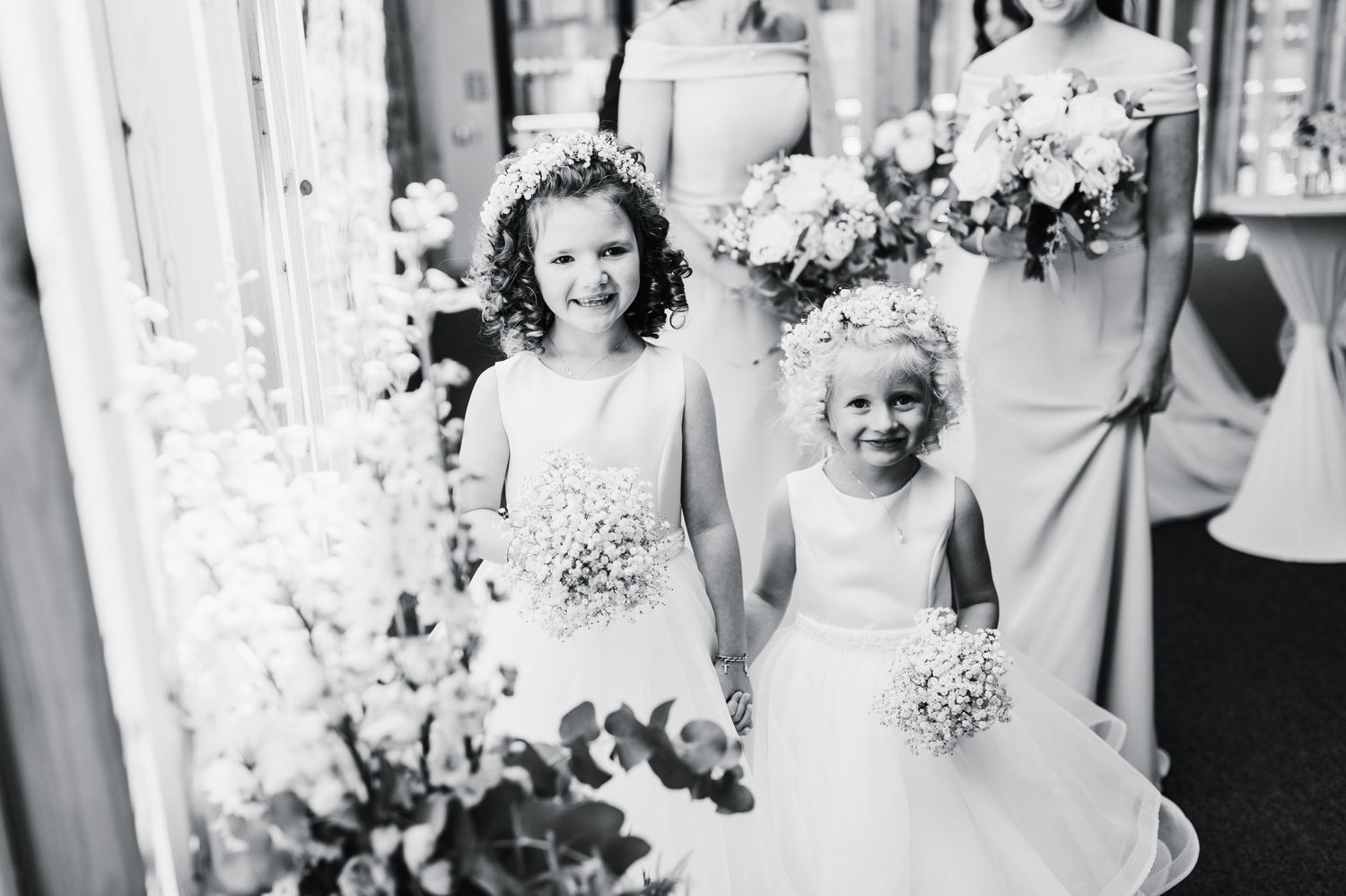 Black and white photo of two flower girls holding bouquets in classic wedding style.