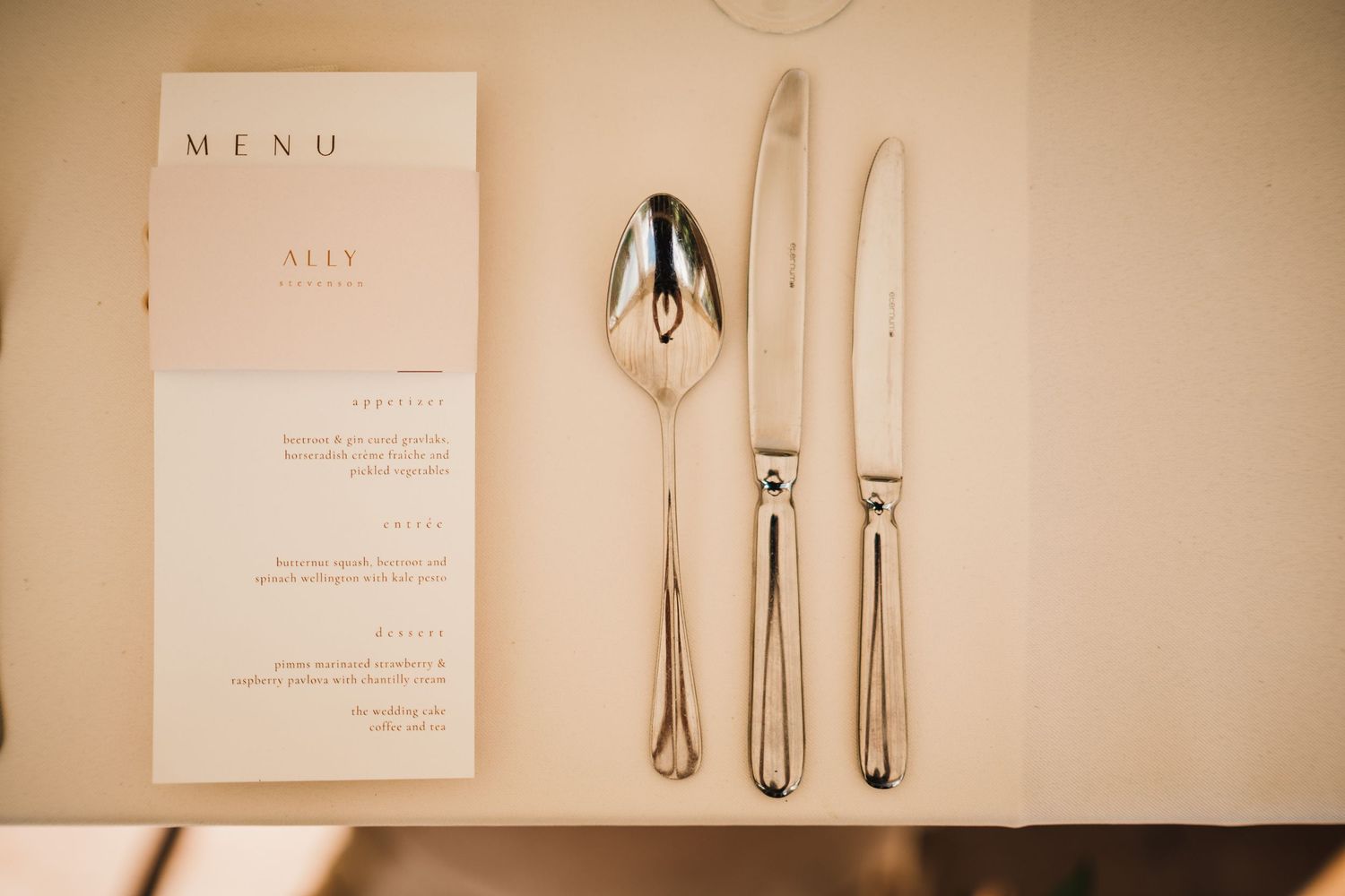 Wedding menu card displayed with elegant silver cutlery on neutral background.
