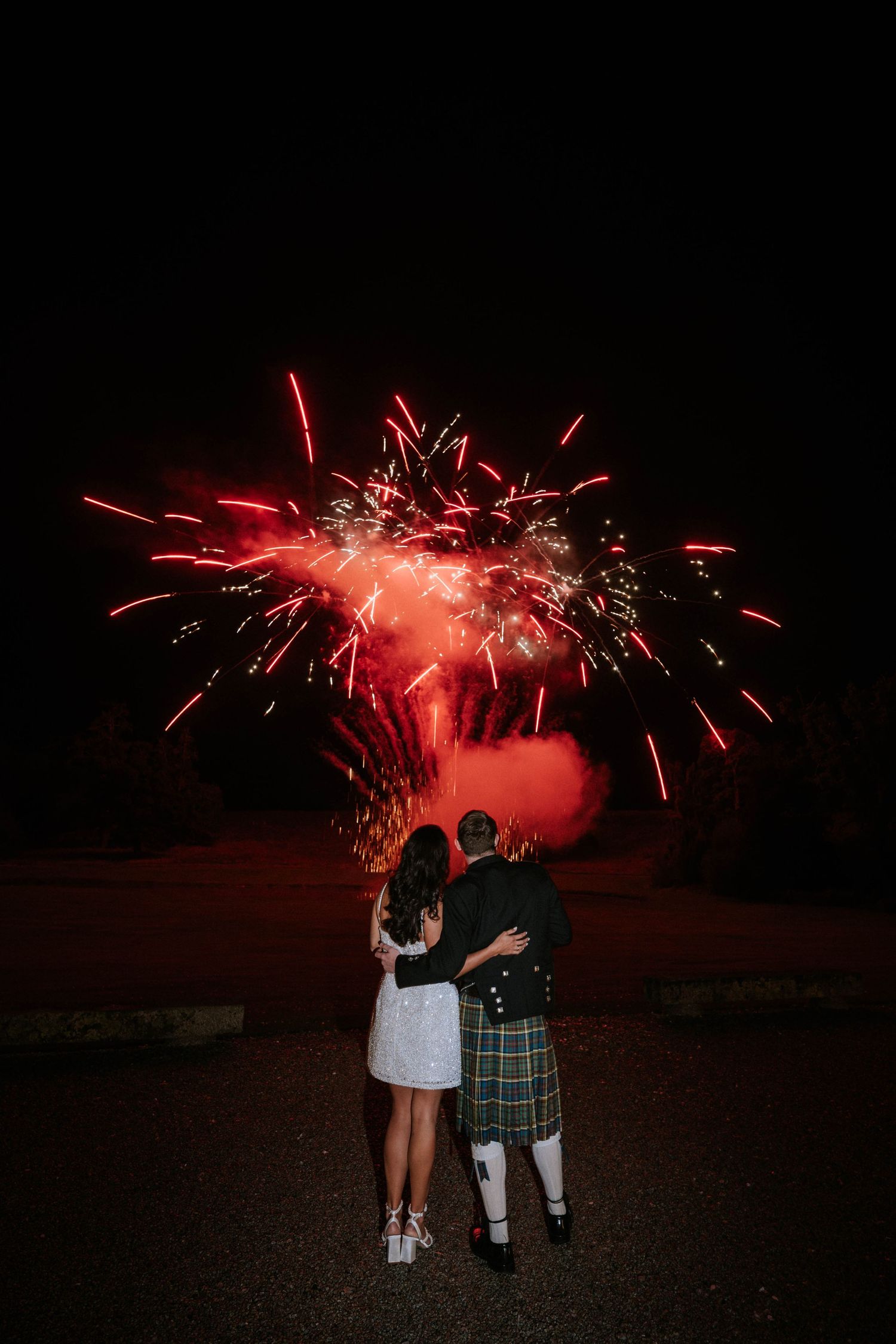 Silhouettes watching red fireworks explode against the dark night sky.