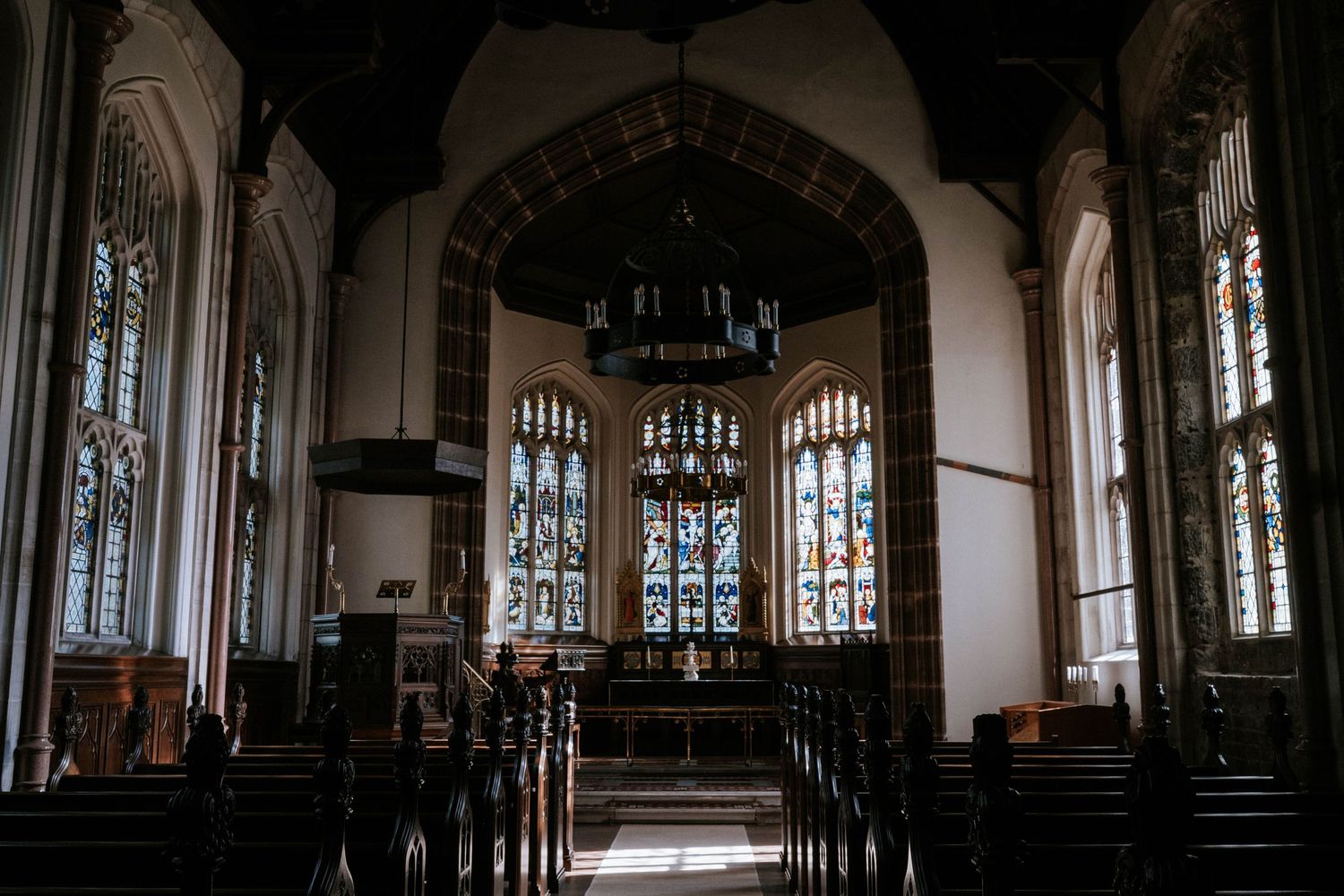 Gothic church interior with vaulted ceilings and stained glass windows creating dramatic lighting.