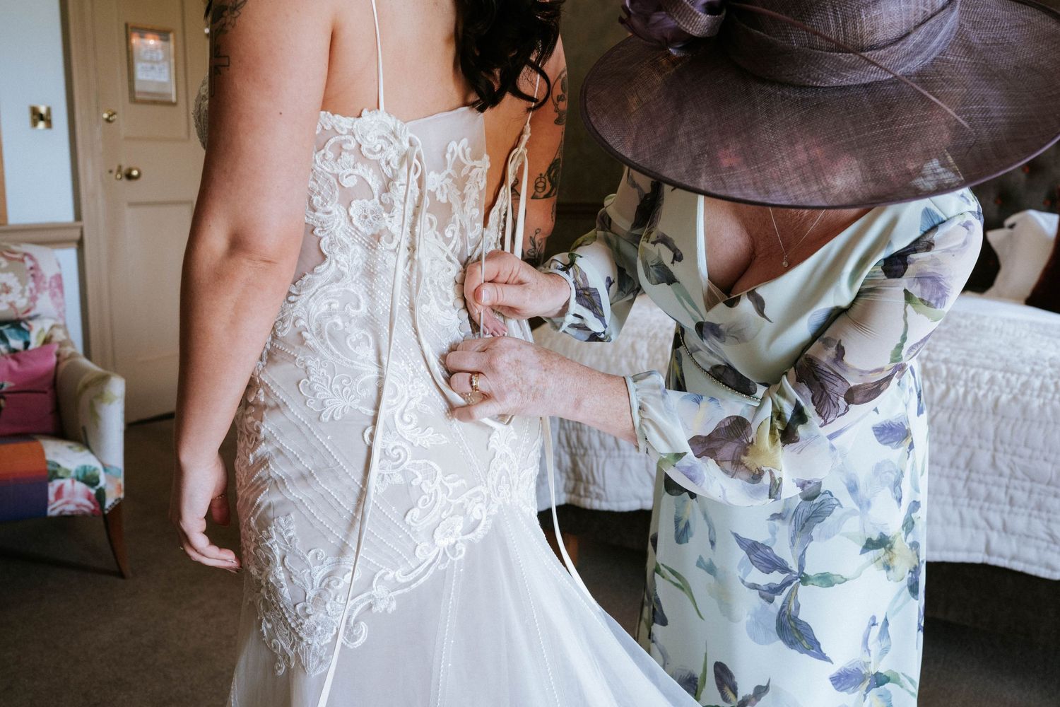 Helper adjusts the back of an intricate lace wedding gown during final preparations.