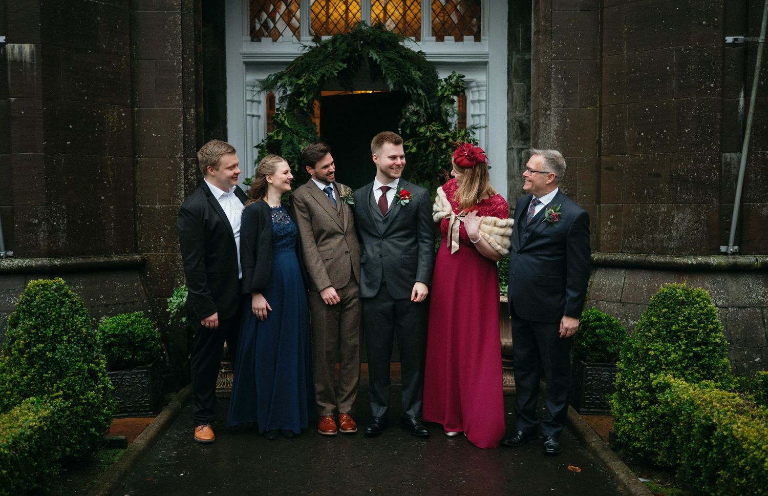 Group poses in formal attire against a brick building backdrop with greenery.