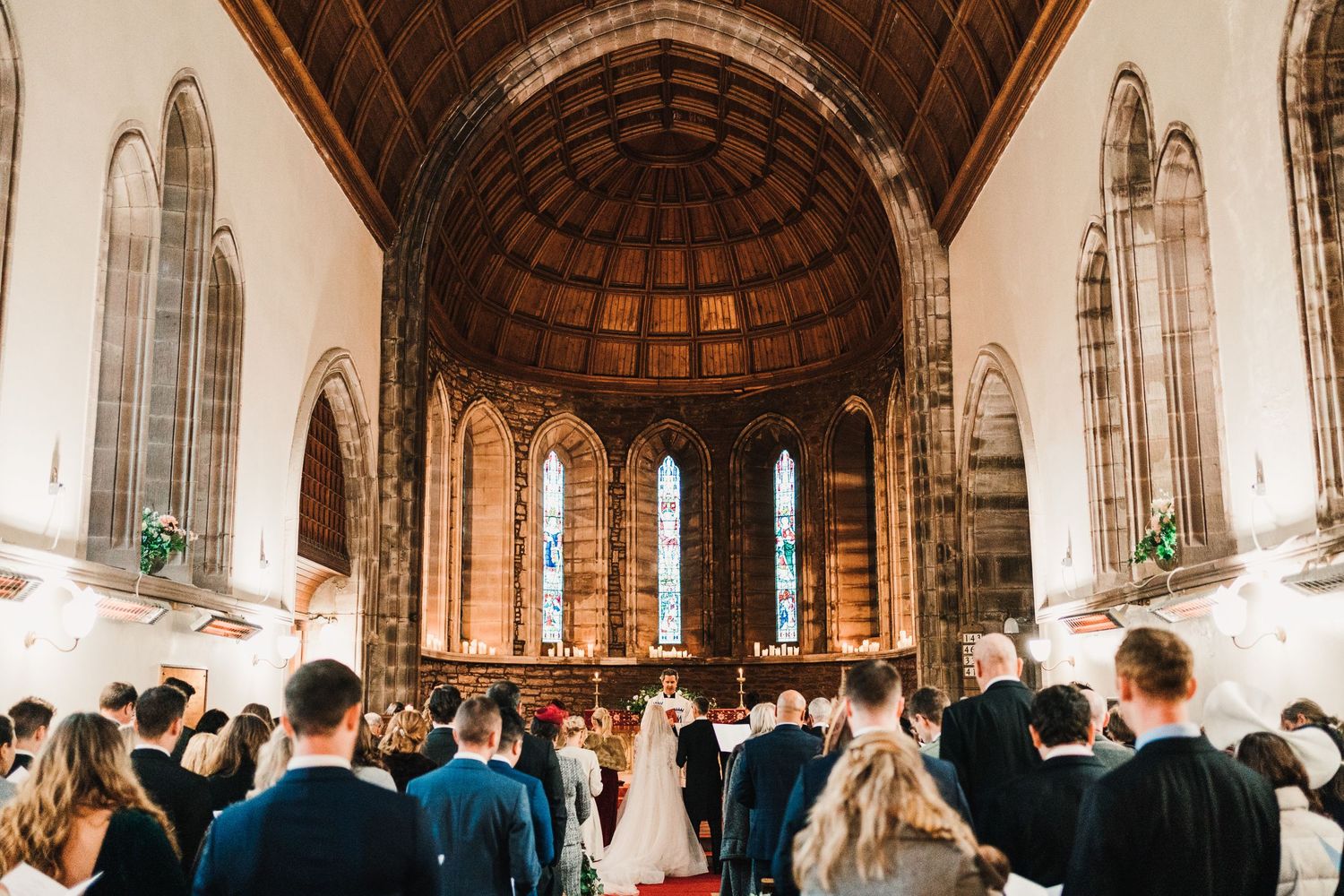 A wedding ceremony unfolds in a historic stone church with vaulted ceilings and tall windows.