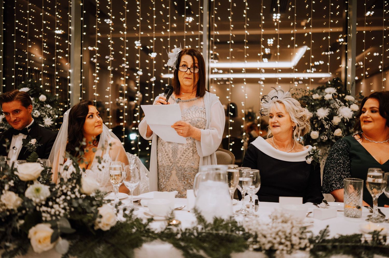 Wedding reception head table decorated with fairy lights and white floral arrangements.
