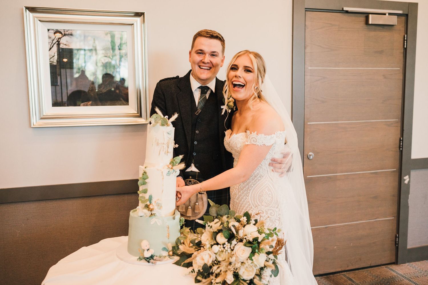 A newlywed couple cuts their elegant white wedding cake together.