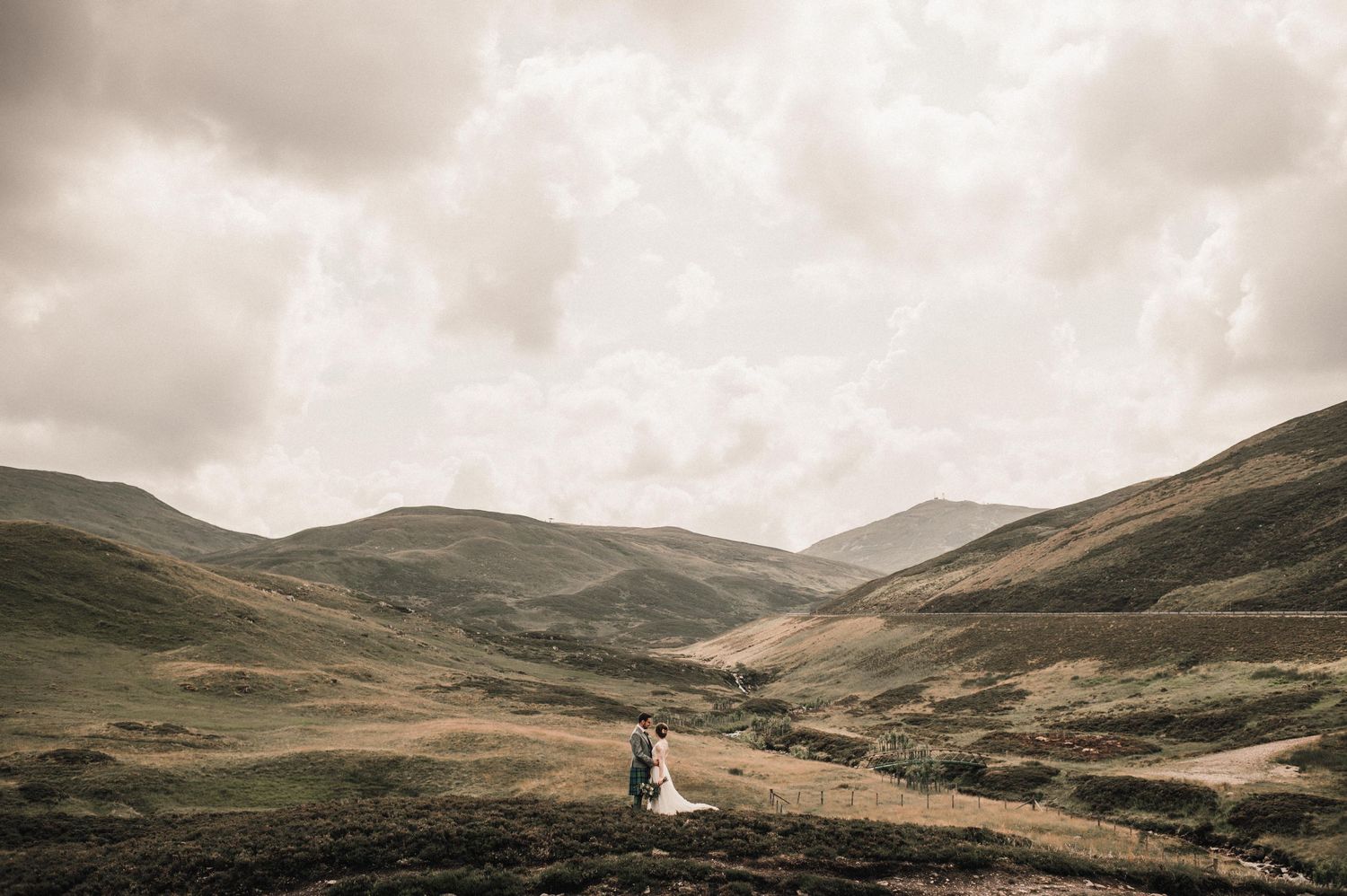 Distant view of wedding couple in vast Scottish Highland valley.