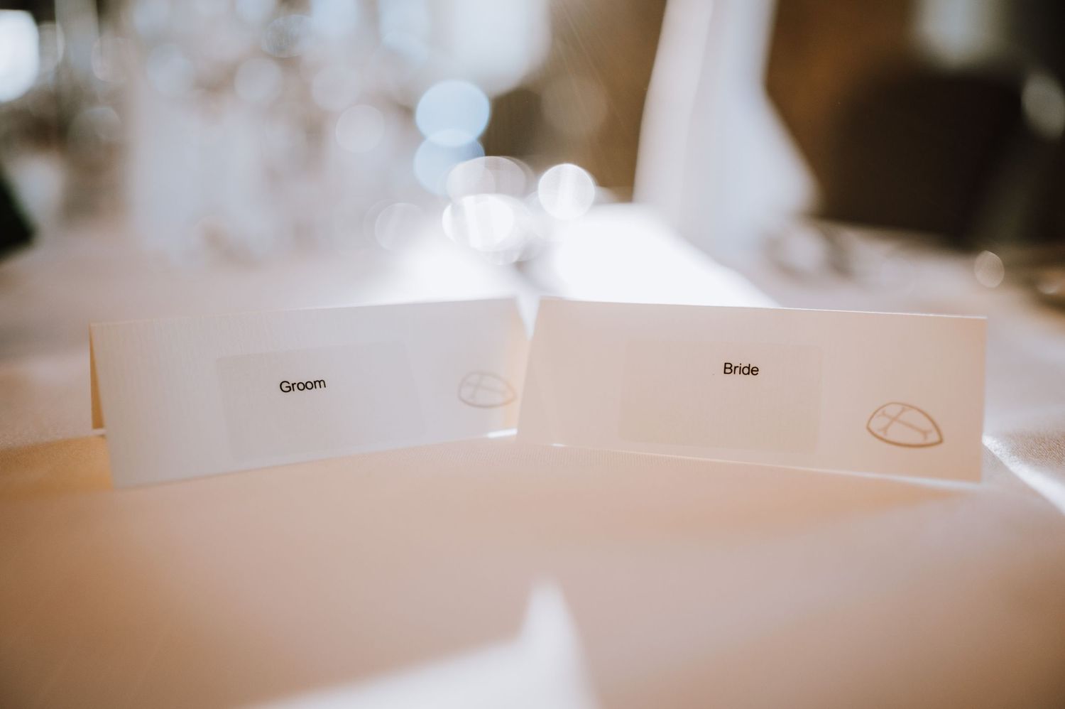 Simple white place cards sit on a wedding reception table with soft focus background.