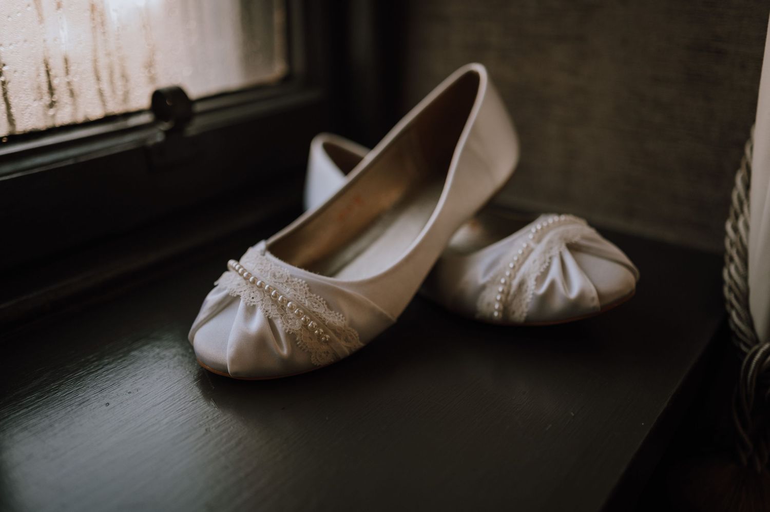 Elegant ivory bridal flats with bow detail positioned by a window.