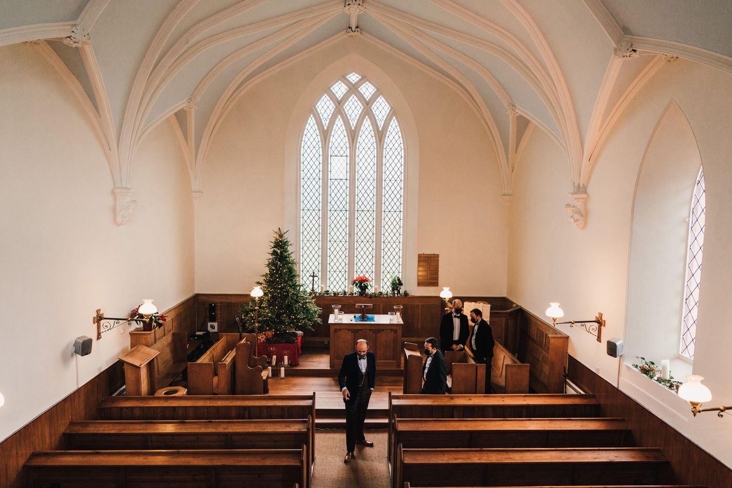Interior of a chapel with vaulted ceilings, wooden pews and Christmas tree near altar.