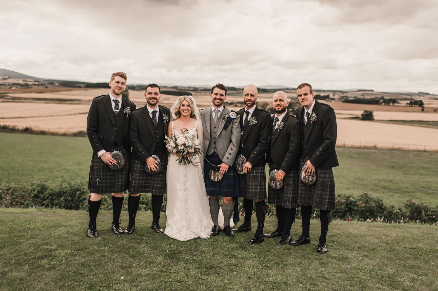 Groomsmen in traditional Scottish kilts stand with couple for formal wedding portrait.