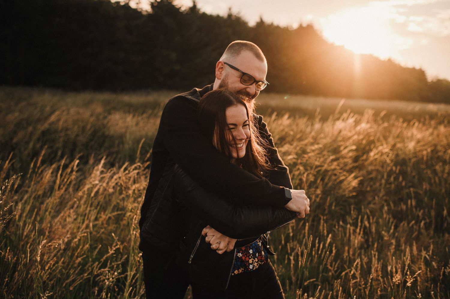 Couple embracing in tall grass field during sunset with warm autumn tones.