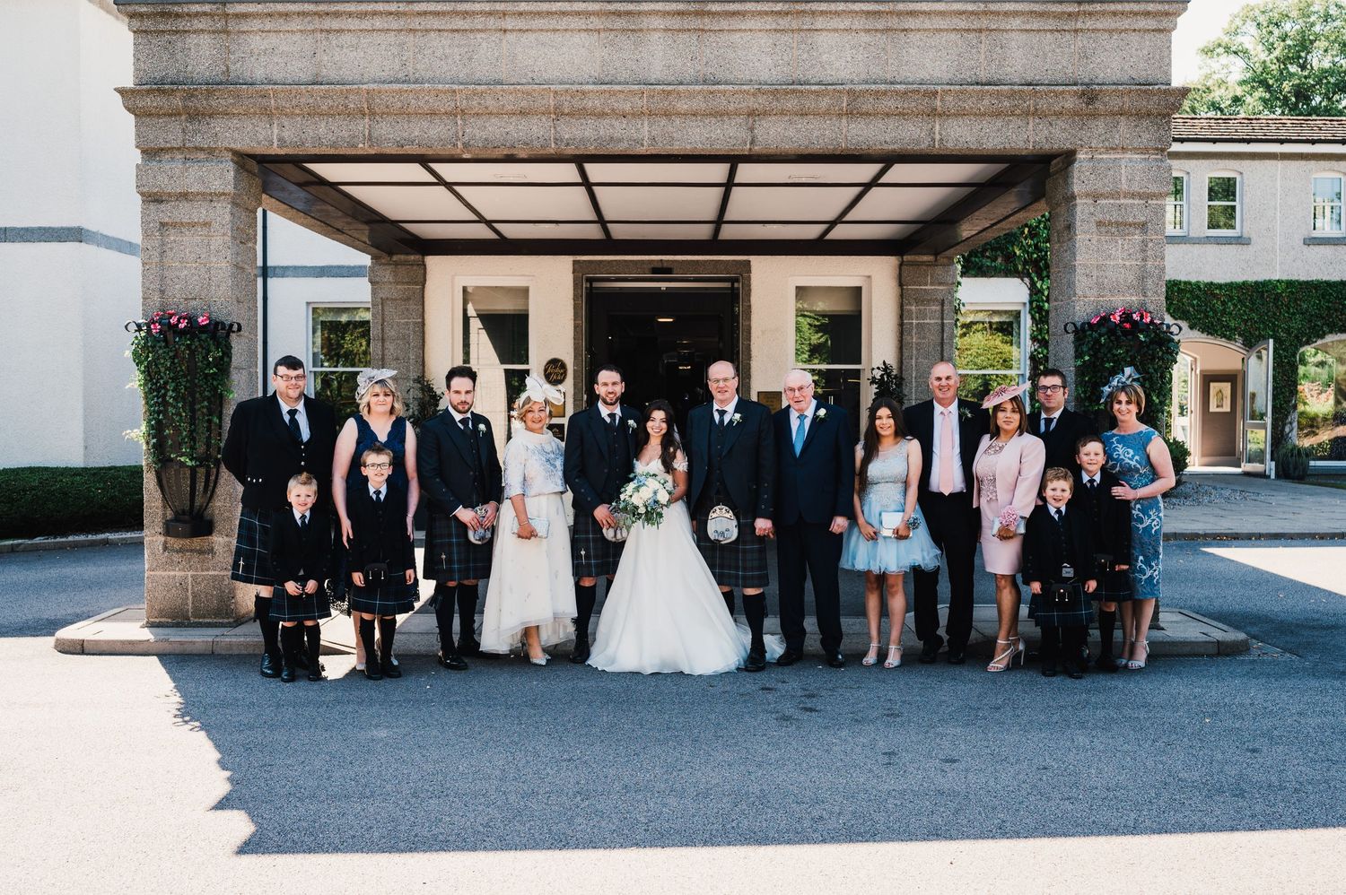 Wedding party and family members gather for formal photo under stone archway entrance.
