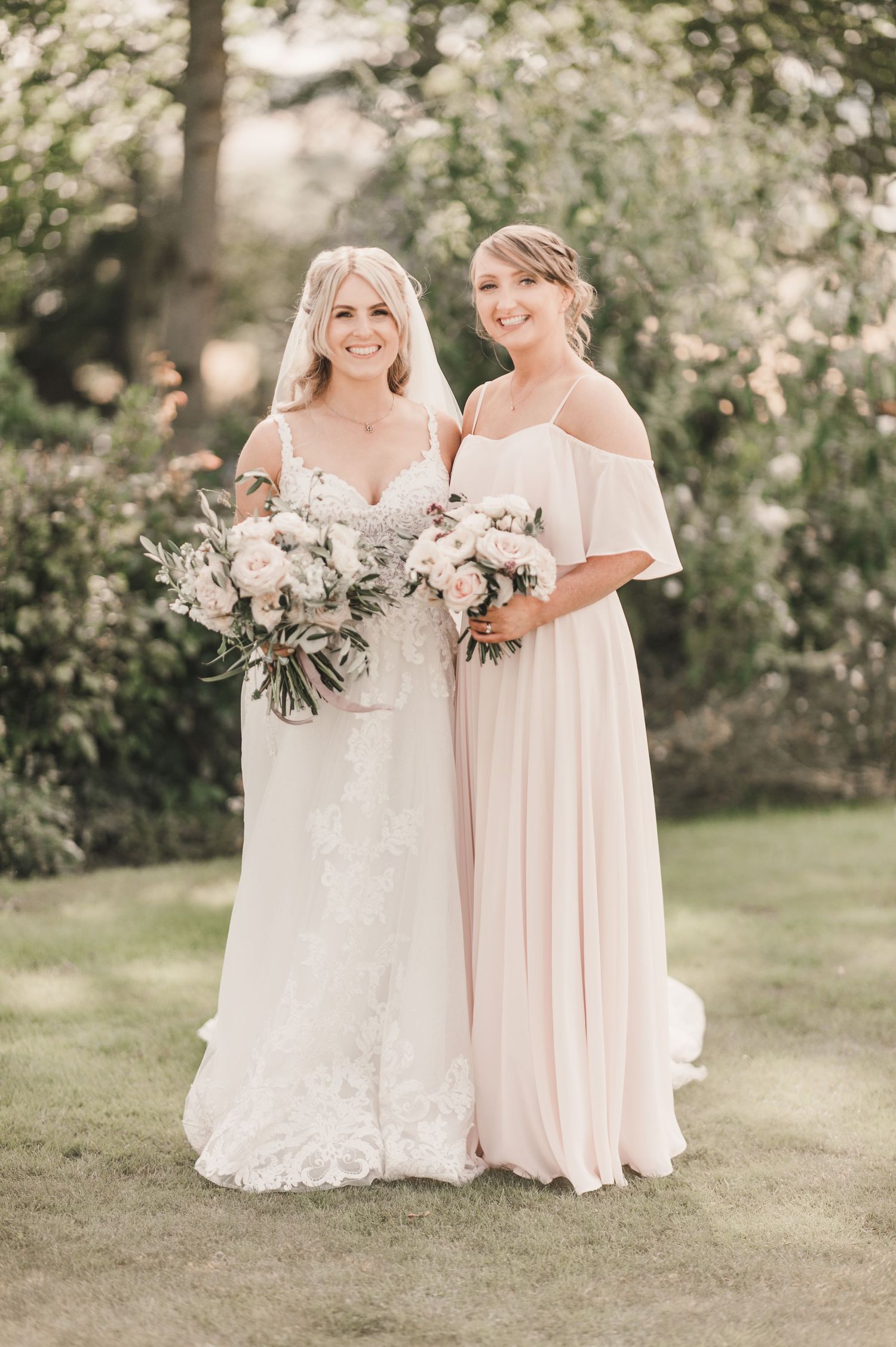 Elegant outdoor wedding portrait with blush bridesmaid dress and white lace bridal gown with matching bouquets.