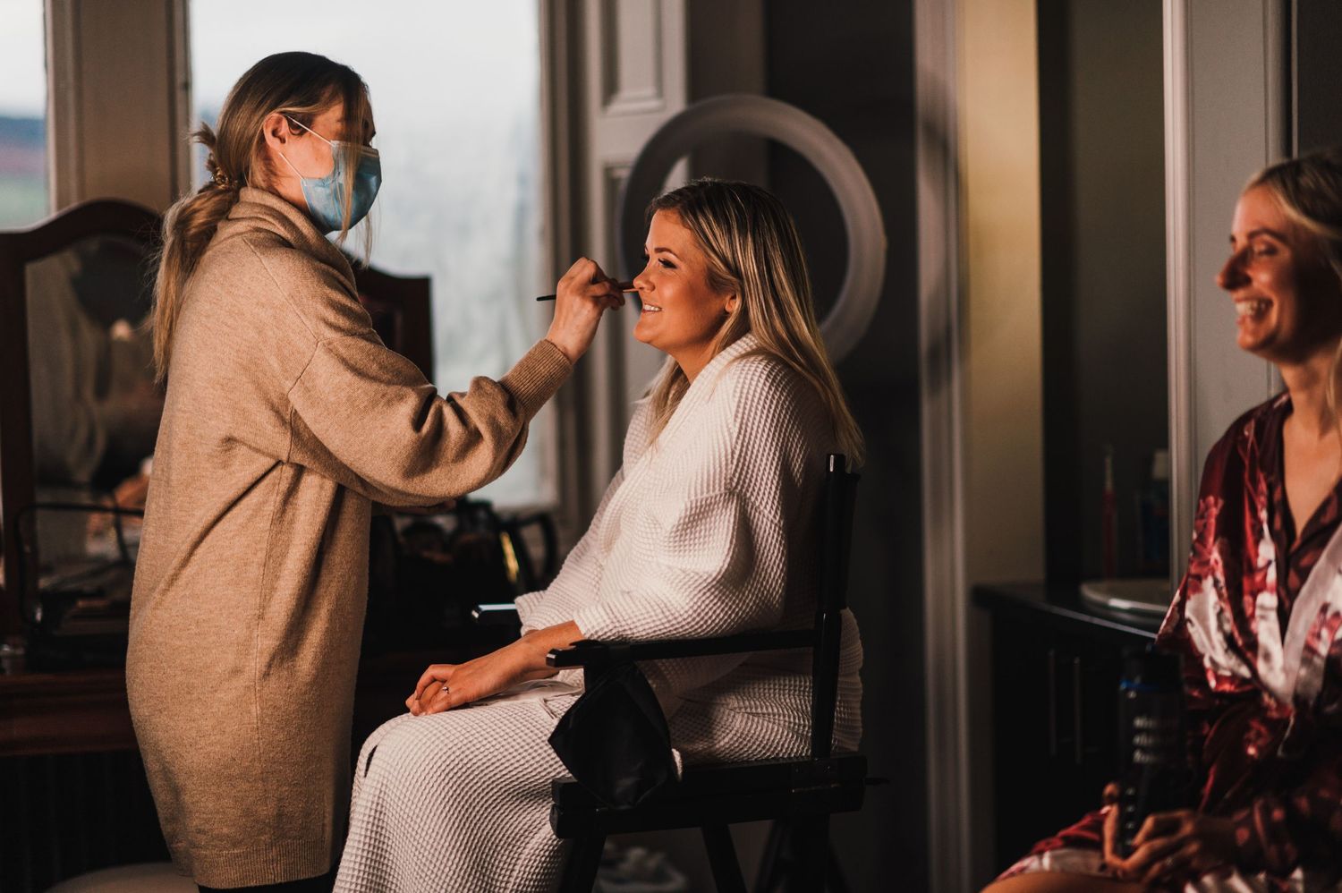 Makeup artist applying cosmetics to someone in a cozy preparation room.