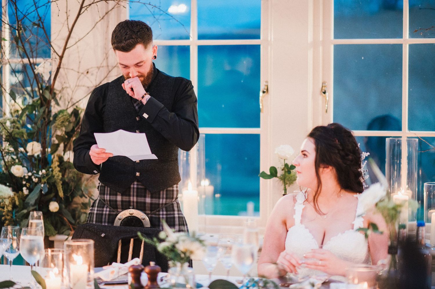 Wedding reception speech moment at elegant dining table with window backdrop.