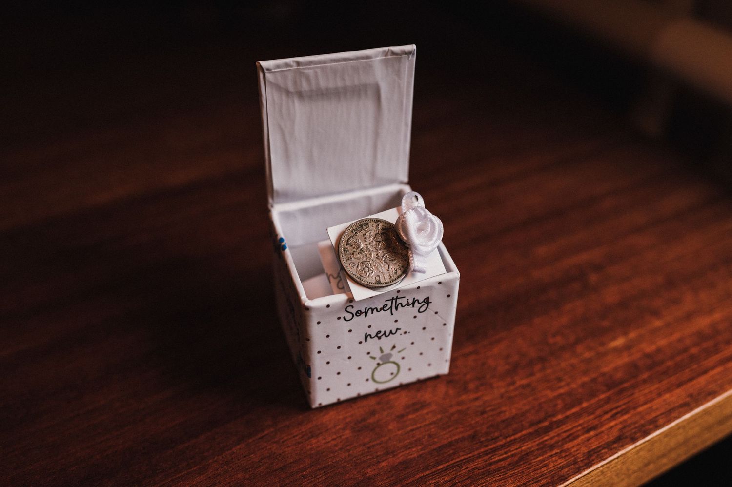 Small white box containing a vintage gold coin sits on dark wooden surface.