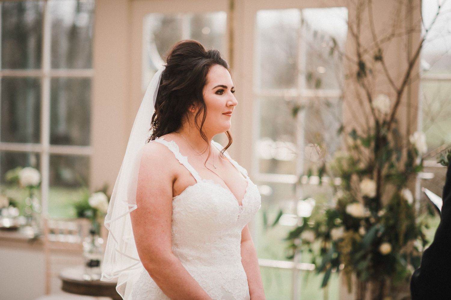 A radiant bride in a classic white wedding gown with veil poses in a sunlit conservatory.