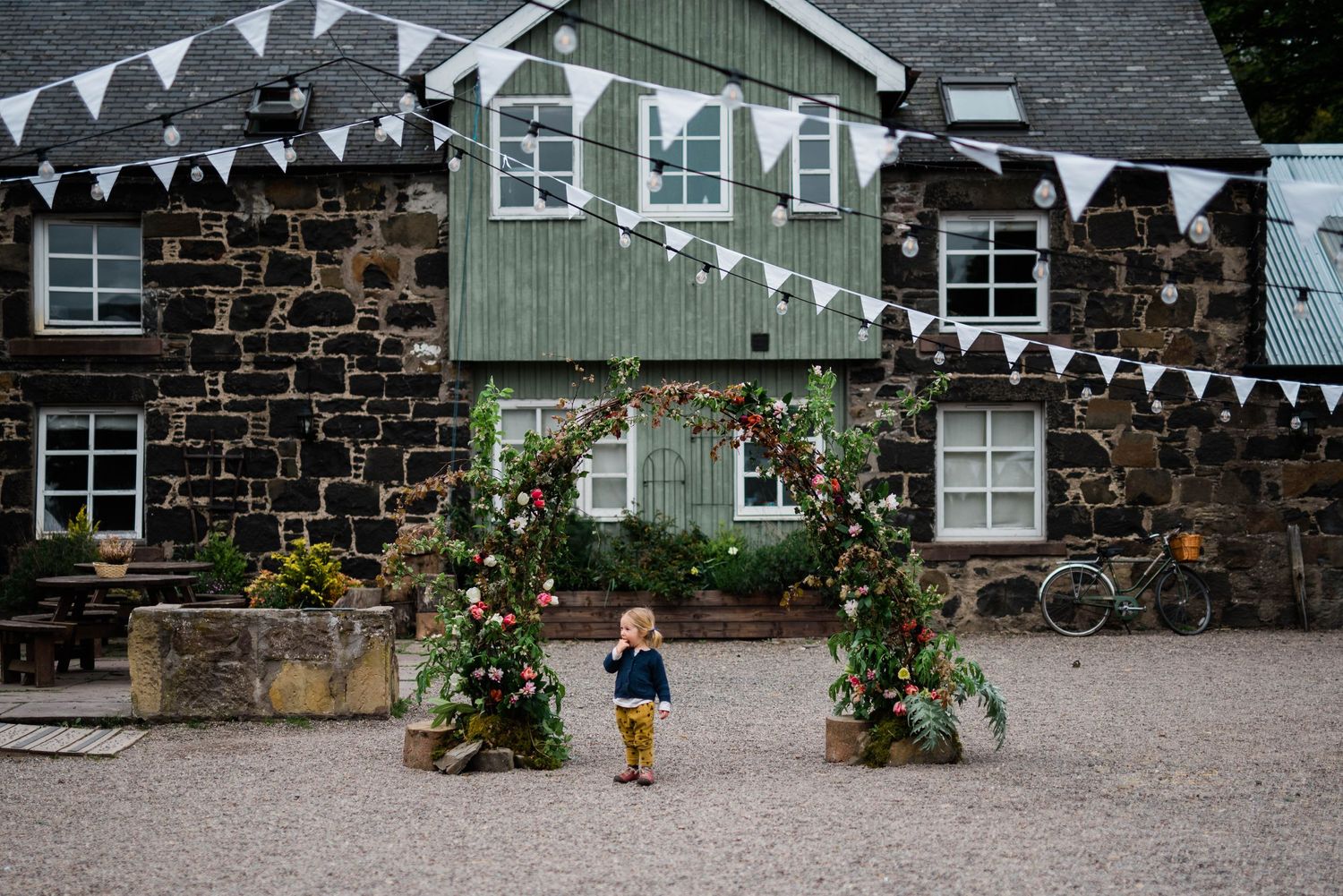 Child walking through decorated courtyard with white bunting and stone building backdrop.