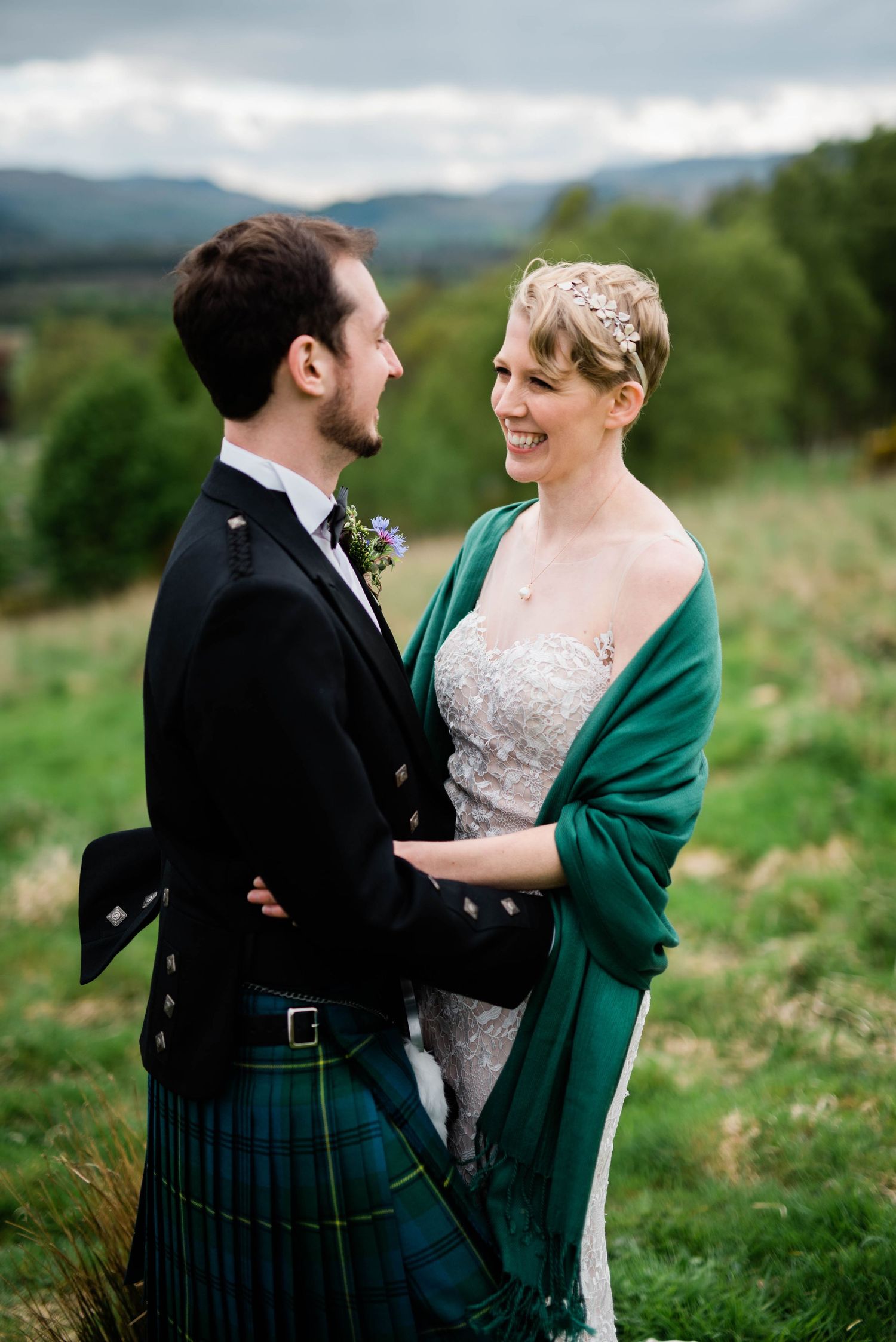 A wedding couple shares an intimate moment on a hillside, with the bride wearing an emerald green wrap.