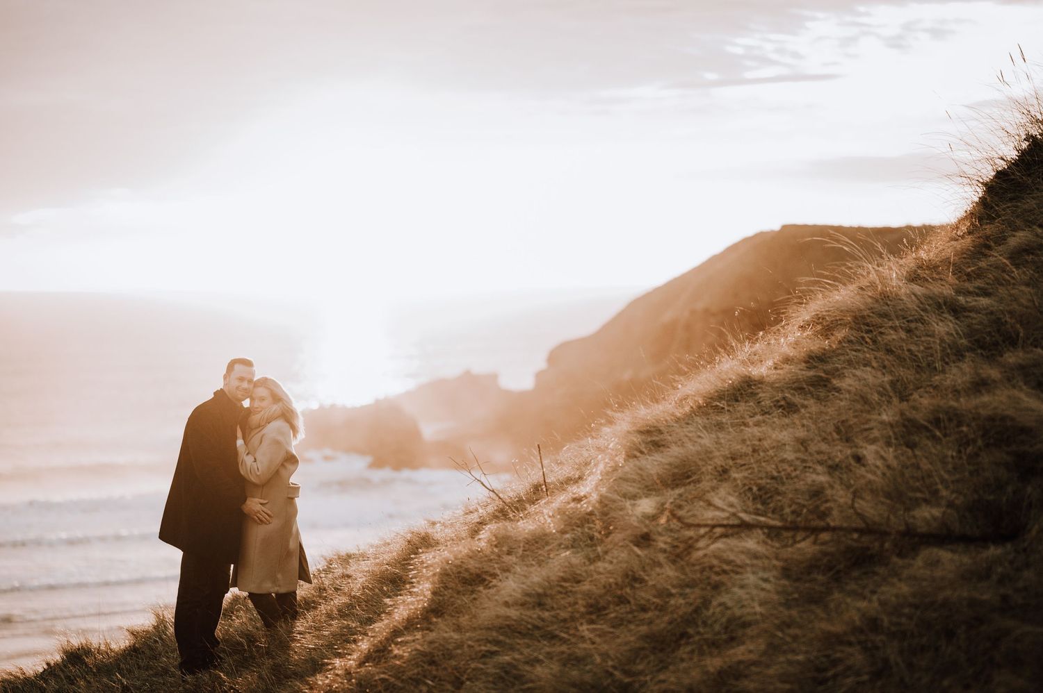 Couple embracing on a misty coastal hillside during sunset at the beach.