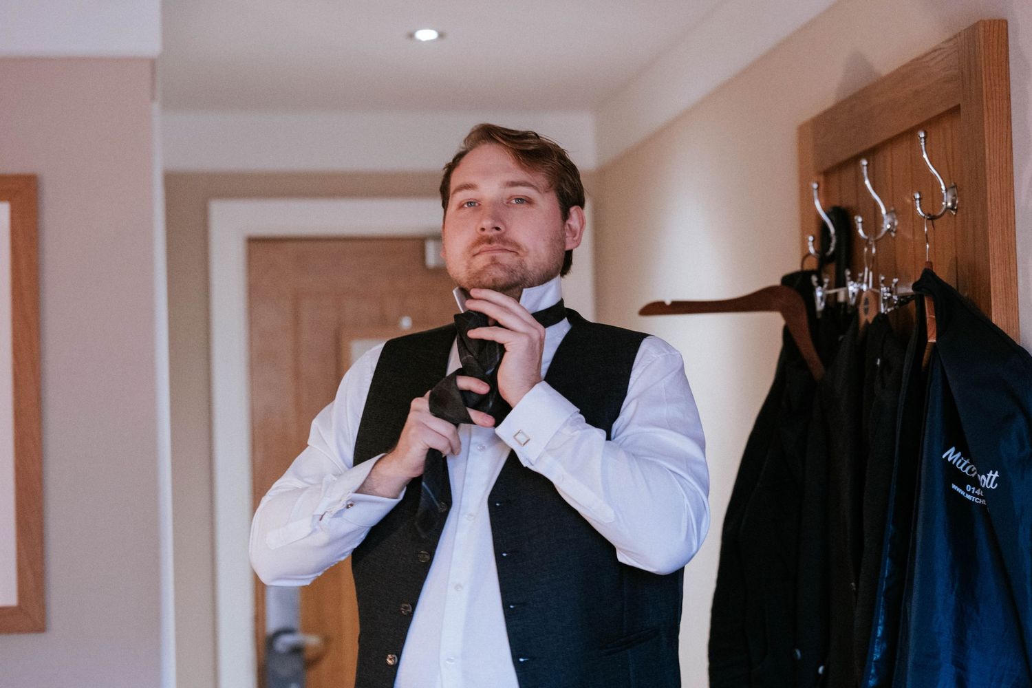 Getting ready scene in bright modern room with formal attire visible in background.
