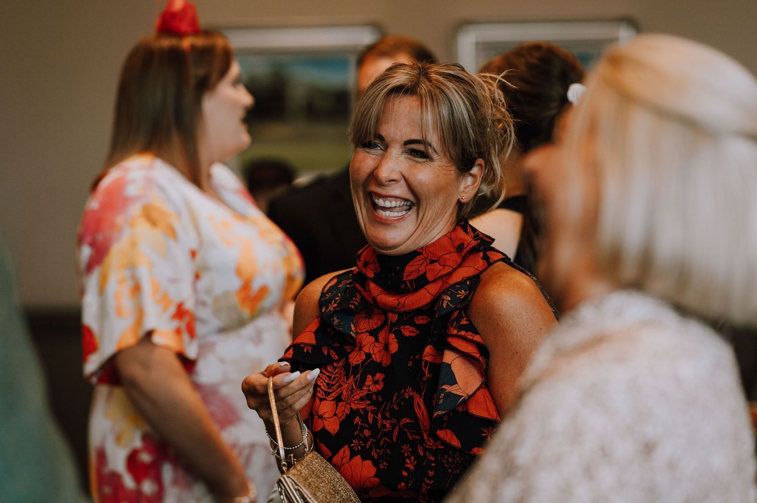Wedding guest in red and black floral dress laughing during reception celebration.