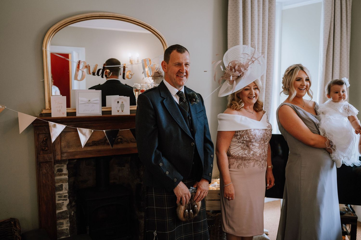 Wedding guests gather in a cozy room with an arched mirror and fireplace during the celebration.