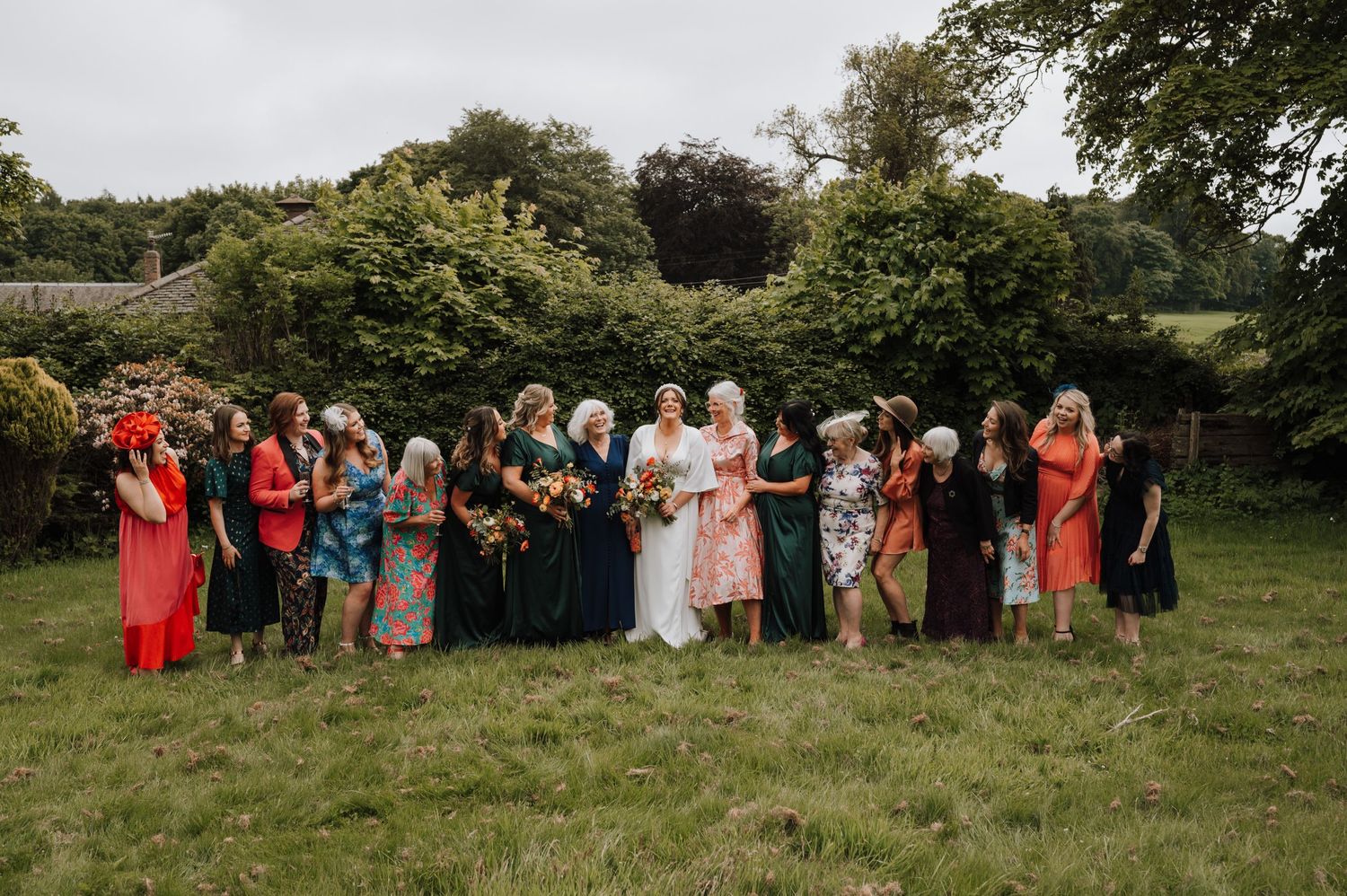 Wedding party in coral and pastel dresses poses together on green lawn.
