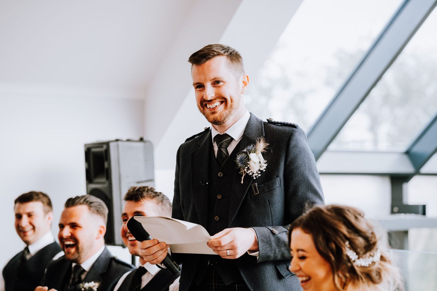 Groom smiling while giving his wedding speech at an elegant reception venue.