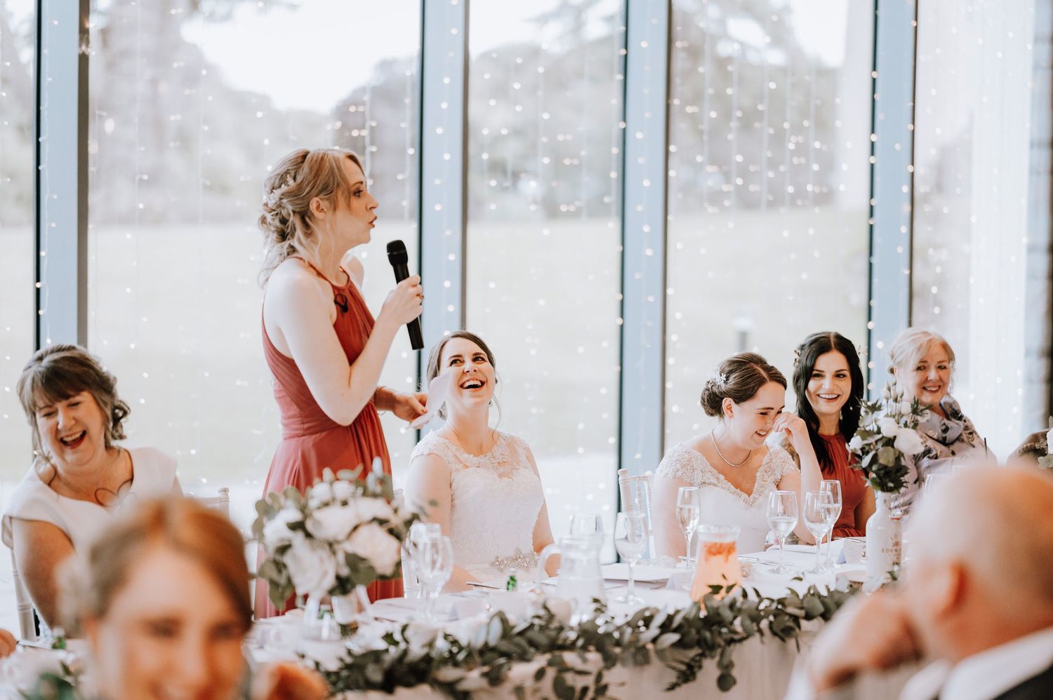 Wedding reception speech moment with snowy backdrop through large windows.
