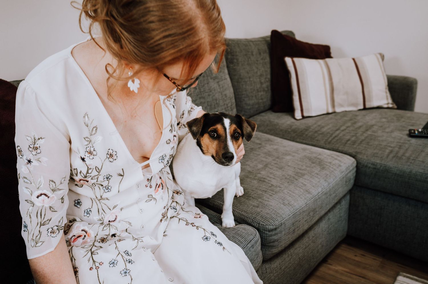 A Jack Russell terrier sitting next to someone in a floral robe on a grey couch.