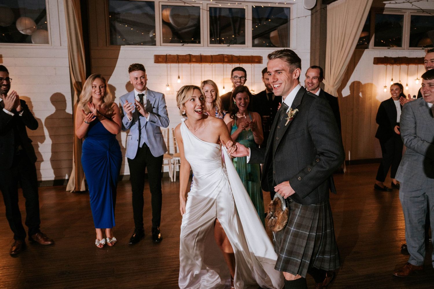 Wedding couple dancing in reception venue while guests watch and applaud.