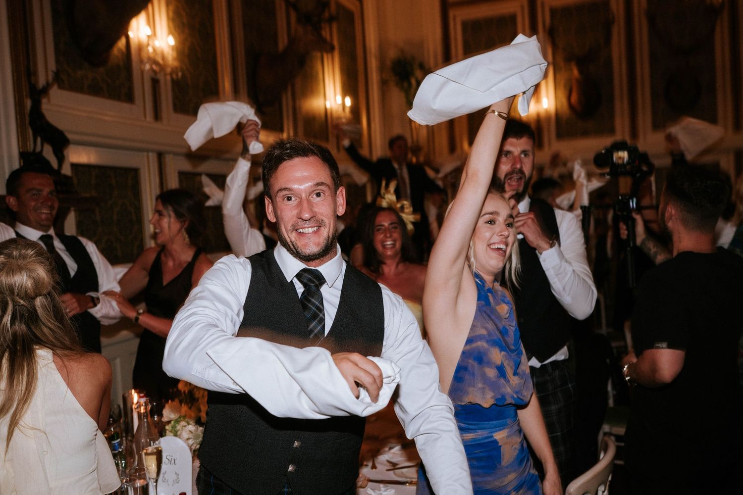 Wedding party celebrates on dance floor with hands raised in joy.