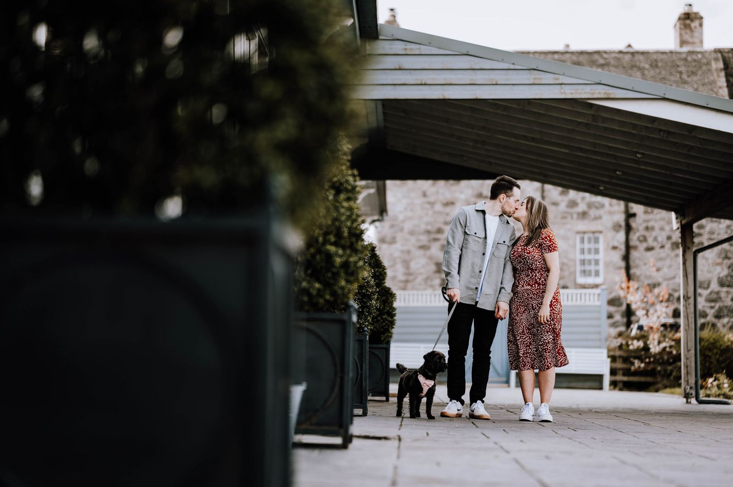 Engagement photography session Aberdeen. A couple poses outside a rustic brick building on a sunny day.