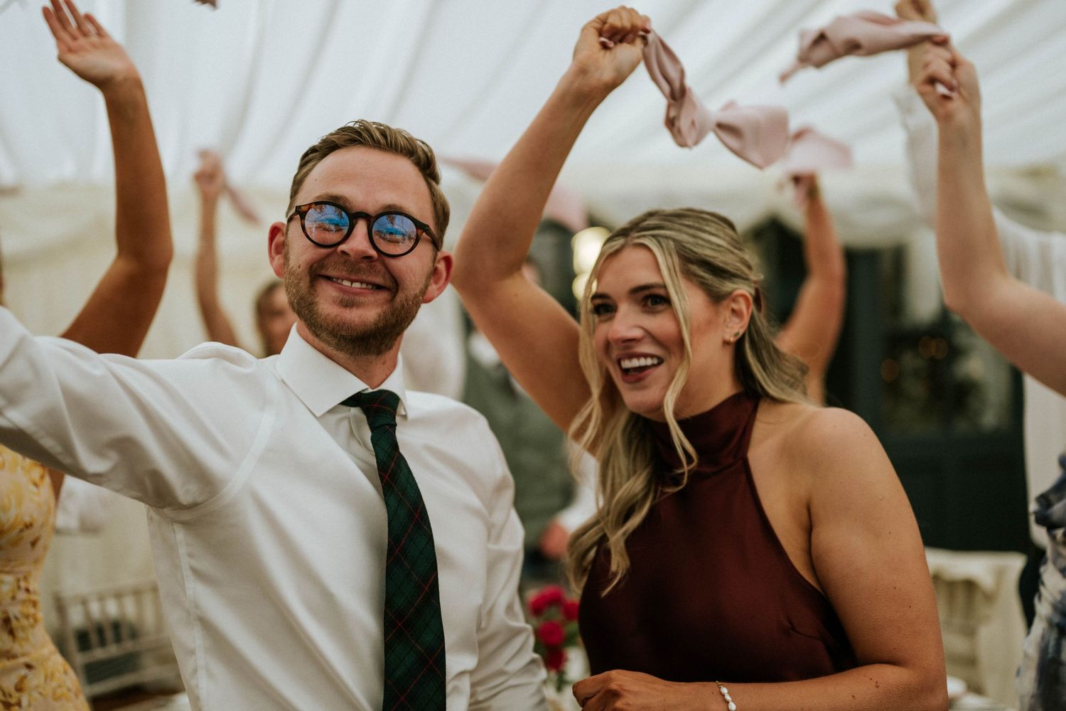 Party guests dancing and celebrating with arms raised at an indoor event.