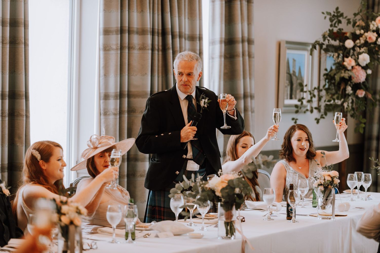 Wedding guests laugh and raise their hands during a speech at an elegant reception banquet.
