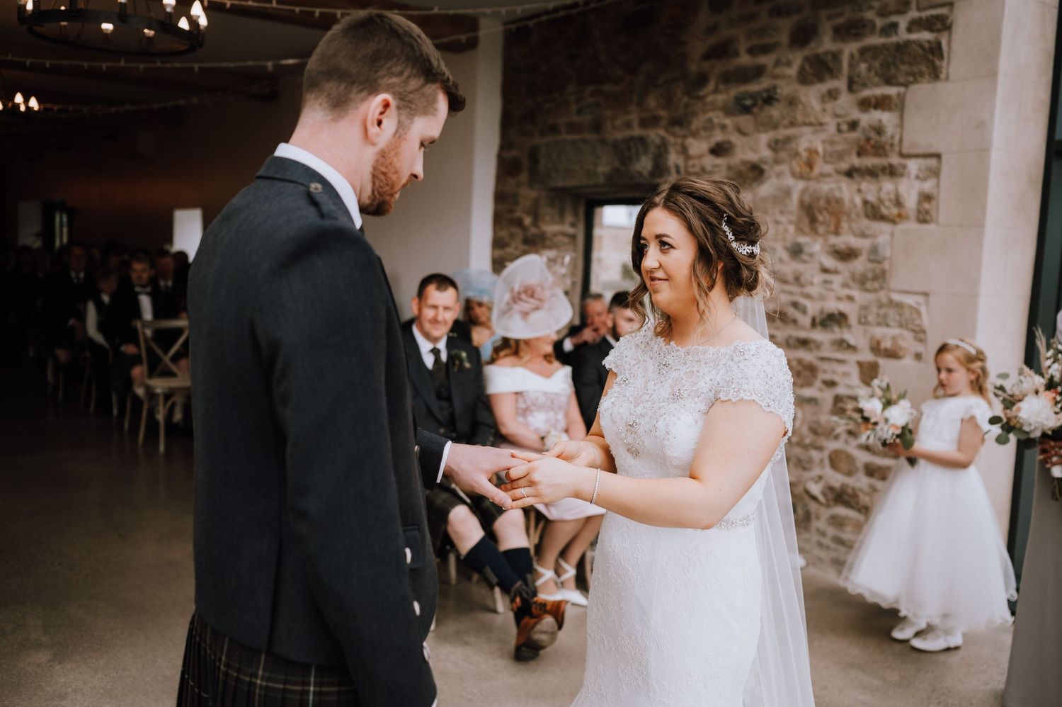 A traditional Scottish wedding ceremony with the couple exchanging rings in front of stone walls.