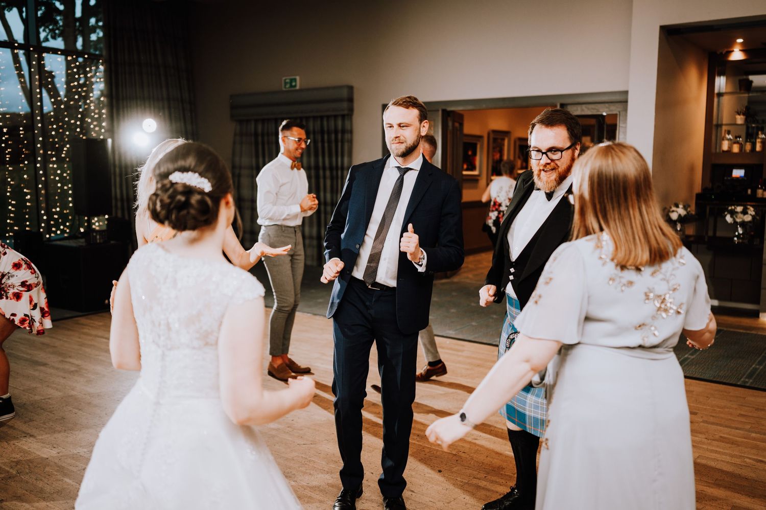 Wedding reception party with guests dancing on wooden floors under decorative lighting.