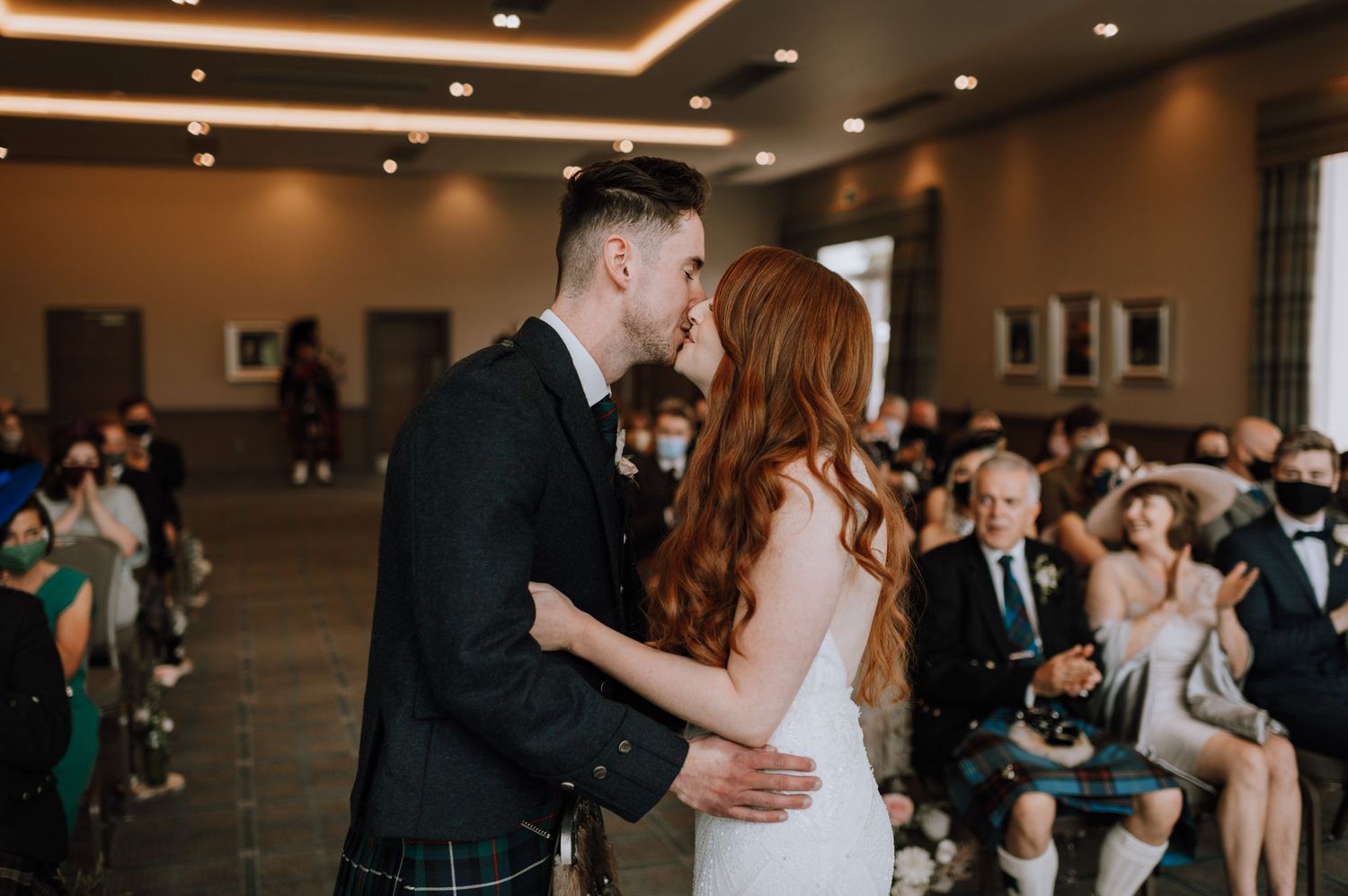 Tender moment shared during an indoor wedding ceremony with guests looking on.