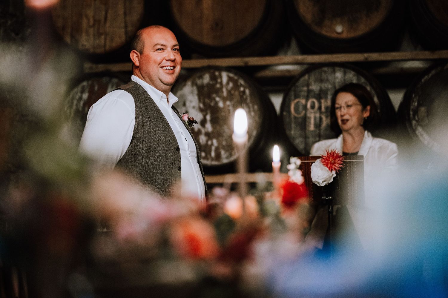 Wedding celebration in a rustic wine cellar with wooden barrels as backdrop.