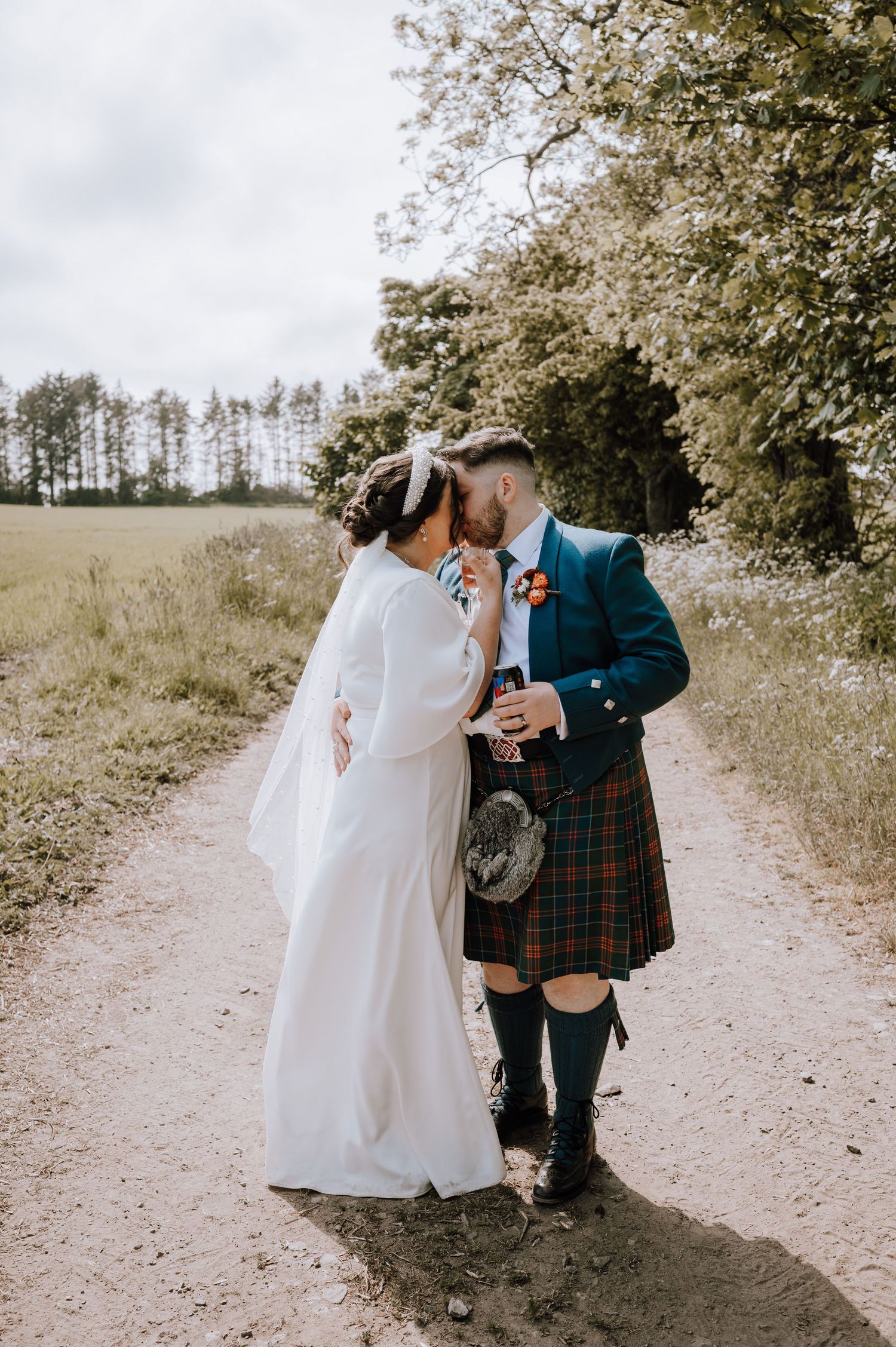 Romantic wedding couple embracing on rural path with traditional Scottish wedding attire.