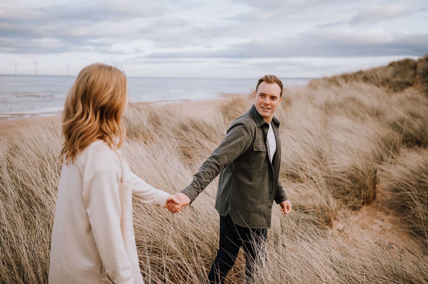 A couple laughs together while walking through tall coastal grass.